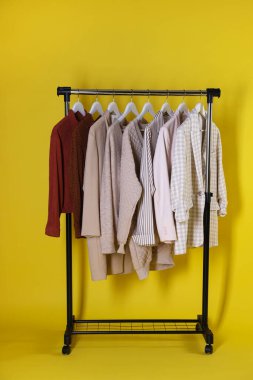 Farklı kadın kıyafetleri sarı arka planda asılı duruyor.