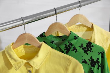 Beyaz duvarın yanında askıda asılı farklı şık kıyafetler, yakın plan.