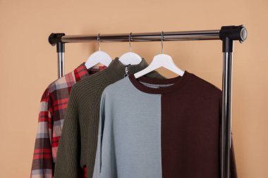 Bej arka planda askıda asılı farklı şık kıyafetler, yakın plan.