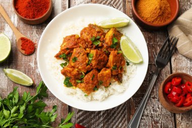 Lezzetli tavuk tikka masala ile pirinç, maydanoz, limon ve baharatlar renkli ahşap masa üzerinde servis edilir, düz yatak