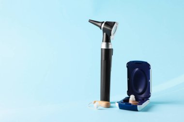 Açık mavi arka planda modern otoskop ve işitme cihazı, yakın plan. Metin için boşluk