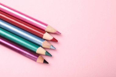 Pembe arka planda parlak göz kalemleri, düz yatış. Metin için boşluk