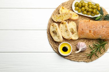 Taze kesilmiş ciabatta, yağ, zeytin, sarımsak ve biberiye beyaz ahşap masa, üst manzara. Metin için boşluk