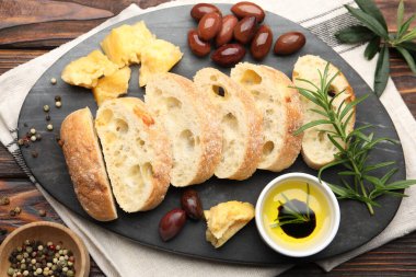 Taze ciabatta, yağ, zeytin, peynir, biberiye ve biber parçaları ahşap masada, düz uzanmış.