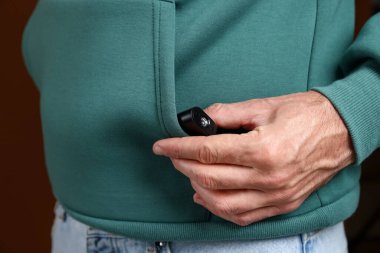 Kahverengi arka planda cebinde gizli casus kamerası olan adam, yakın plan.