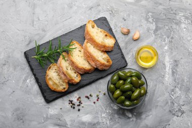 Ciabatta dilimleri, gri masada baharatlar ve zeytinler.