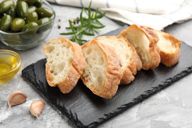 Ciabatta dilimleri, baharatlar ve zeytinler gri masada, yakın plan.