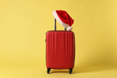Sarı arka planda Noel Baba şapkası olan şık bir bavul. Noel tatili