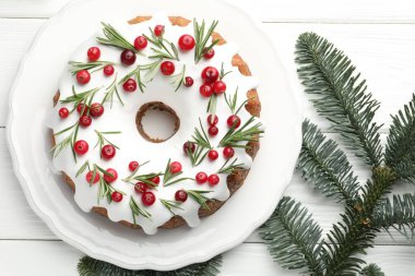 Beyaz ahşap masa üzerinde kremalı, kızılcıklı, biberiyeli ve köknar ağacı dallı lezzetli bir Noel pastası.