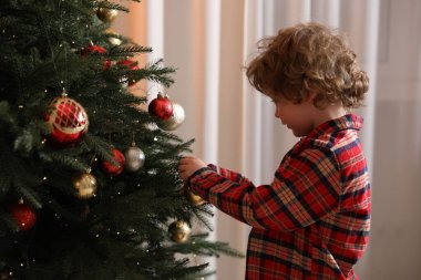 Pijamalı küçük çocuk evde Noel ağacı süslüyor.