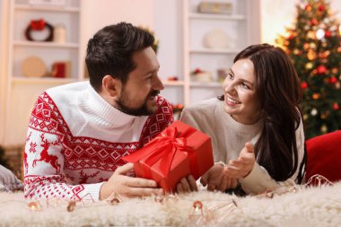 Hediye kutusu olan mutlu çift Noel için dekore edilmiş odada birlikte vakit geçiriyor.