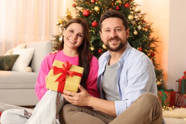 Hediye kutusu olan mutlu çift Noel için dekore edilmiş odada birlikte vakit geçiriyor.