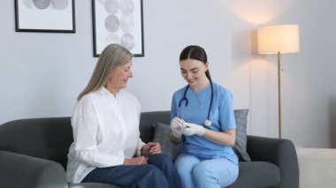 Diyabet. Tıbbi eldivenli gülümseyen doktor evdeki kanepede neşter ve glukometreyle hastanın kan şekerini ölçüyor. Kamera ilerliyor.