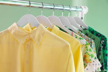 Farklı kadın kıyafetleri yeşil arka planda asılı, yakın plan.