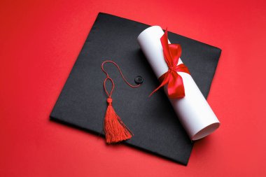 Kırmızı arka planda diploma ve mezuniyet şapkası.