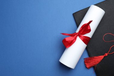 Mavi arka planda diploma ve mezuniyet şapkası, üst manzara. Metin için boşluk