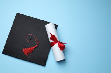 Açık mavi arka planda diploma ve mezuniyet şapkası, üst manzara. Metin için boşluk