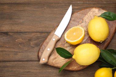Bir bütün, yeşil yapraklı limonlar ve tahta masada bıçak, düz yatış. Metin için boşluk