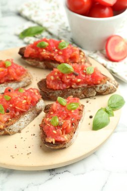 Domatesli lezzetli bruschettalar ve beyaz mermer masada fesleğen, yakın plan.