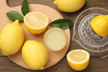 Bardakta limon suyu, yapraklar, meyve sıkacağı ve ahşap masada taze limon.