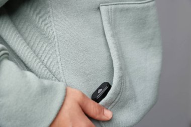 Cebinde gizli kamera olan genç bir kadın açık gri arka planda, yakın plan.