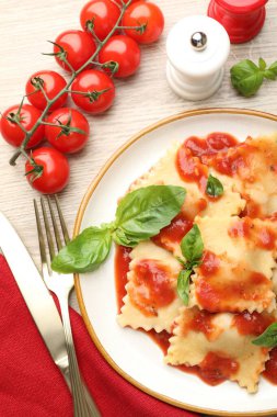 Hafif ahşap masada servis edilen domates soslu ve fesleğenli lezzetli ravioli.