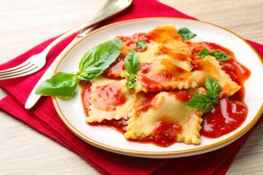 Hafif ahşap masada servis edilen domates soslu ve fesleğenli lezzetli ravioli.