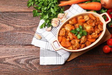 Pişirme kabında nefis pişirilmiş güveç ve ahşap masada taze malzemeler, düz yatak. Metin için boşluk