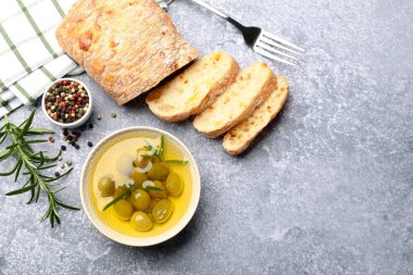 Taze kesilmiş ciabatta, yağ, zeytin, biberiye ve biberiyeler gri desenli masa, düz yatak. Metin için boşluk