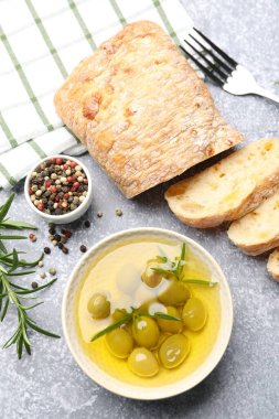 Taze kesilmiş ciabatta, yağ, zeytin ve biberler gri desenli masada, düz yerde.