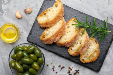 Ciabatta dilimleri, gri masada baharatlar ve zeytinler.