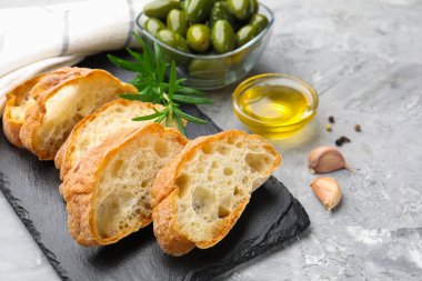 Ciabatta dilimleri, baharatlar ve zeytinler gri masada, yakın plan.