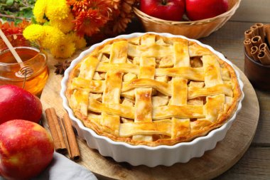 Lezzetli ev yapımı turta, taze elmalar, bal ve çiçekler ahşap masada, yakın plan.