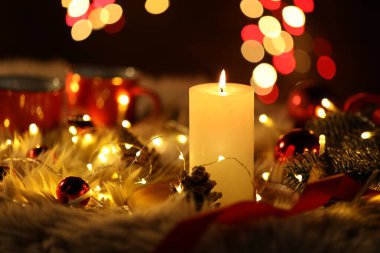 Yanan mumlar, köknar ağacı dalları, takılar, koniler ve sahte kürkün üzerindeki şenlikli ışıklar siyah arka plana karşı bulanık ışıklar, yakın çekim. Bokeh etkisi