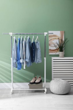 İçerideki yeşil duvarın yanında askıda asılı farklı şık elbiseler, puf ve bitkiler.