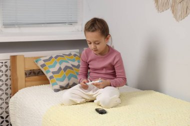 Diyabet. Küçük kız kan şekeri seviyesini kontrol ediyor. Yatağın içinde tükenmez kalemle.