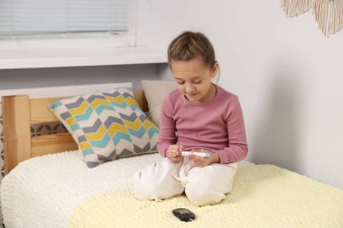 Diyabet. Küçük kız kan şekeri seviyesini kontrol ediyor. Yatağın içinde tükenmez kalemle.