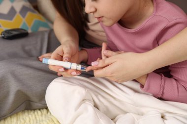 Diyabet. Anne kızının kan şekerini kontrol ediyor. Yatakta tükenmez kalemle, yakın plan.