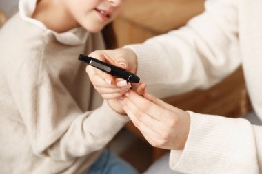 Diyabet. Anne, kızın kan şekerini kontrol ediyor. Kapalı alanda tükenmez kalemle, yakın plan.