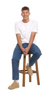 Beyaz arka planda taburede şık kotlar giyen yakışıklı genç adam.