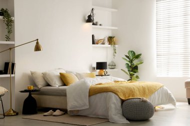 Yatak odasındaki beyaz duvarın yanında çarşafları, komodinleri ve lambaları olan büyük bir yatak.