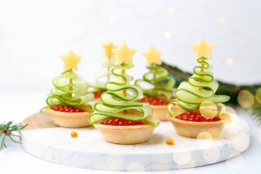 Kırmızı havyar, salatalık, peynir ve beyaz masa üzerindeki şenlikli dekordan yapılmış Noel ağacı şekilli turtalar.