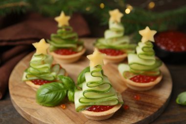 Noel ağacı şeklinde turtalar, kırmızı havyar, salatalık ve peynirle ahşap masada, yakın plan.