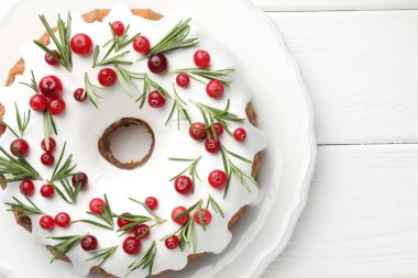 Beyaz ahşap masa üzerinde kremalı, kızılcıklı ve biberiyeli lezzetli bir Noel pastası.