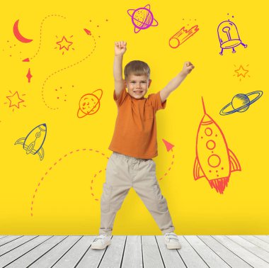 Çocuklar için bilim. Sevimli küçük çocuk kendini evrende uçarken hayal et. Uzay temalı çizimleri olan sarı duvar