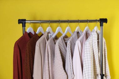 Farklı kadın kıyafetleri sarı arka planda asılı duruyor.