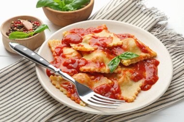 Beyaz ahşap masada servis edilen domates soslu ve fesleğenli lezzetli ravioli.