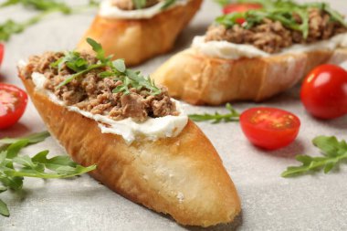 Ton balıklı lezzetli bruschettalar, domatesler ve roka gri masada, yakın plan.