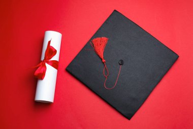 Kırmızı arka planda diploma ve mezuniyet şapkası, üst görünüm