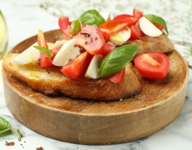 Mozarella peynirli lezzetli bruschettalar, beyaz mermer masada domates ve fesleğen, yakın plan.